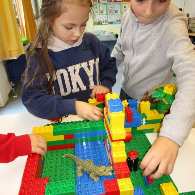 Ein 6jähriger Junge am rechten Bildrand spielt mit einem Zoo aus Lego Duplo. Er hält ein Männchen in der Hand. In den Gehegen sind ein Pinguin und mehrere Affen.