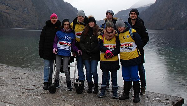 Frau Gauch, Marija, Julian, Frau Fecke, Florian, Lara, Christopher und Herr Kling stehen vor dem Königssee und lächeln in die Kamera. Hinter dem See sind wolkenverhangene Berge zu sehen.