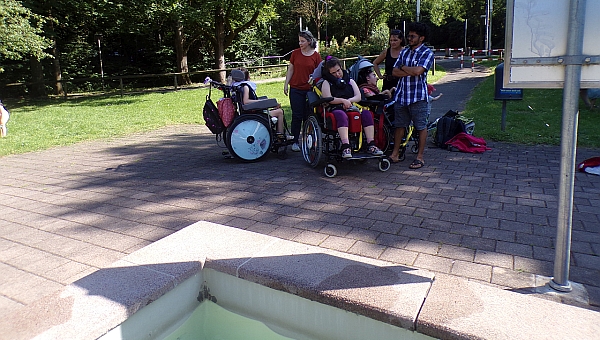 Drei Schüler im Rollstuhl, drei Betreuer stehen gespannt vor dem Kneippbecken