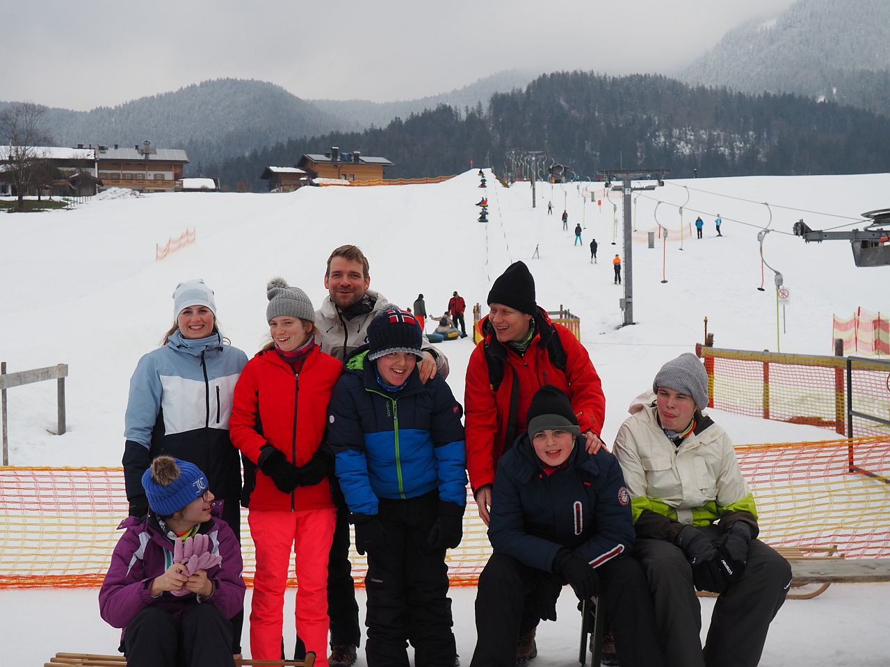 Die fünf Schüler:innen und die drei Lehrpersonen stehen vor dem Snowtubinglift und lachen in die Kamera. 