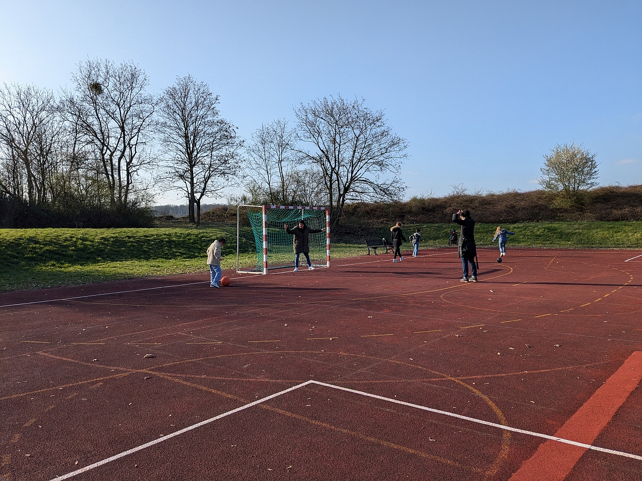 Mehrere Kinder und Erwachsene stehen auf einem Sportplatz und spielen Fußball.