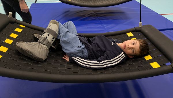 Ein Junge liegt in der Turnhalle auf einer großen Netzschaukel und schaut in die Kamera.
