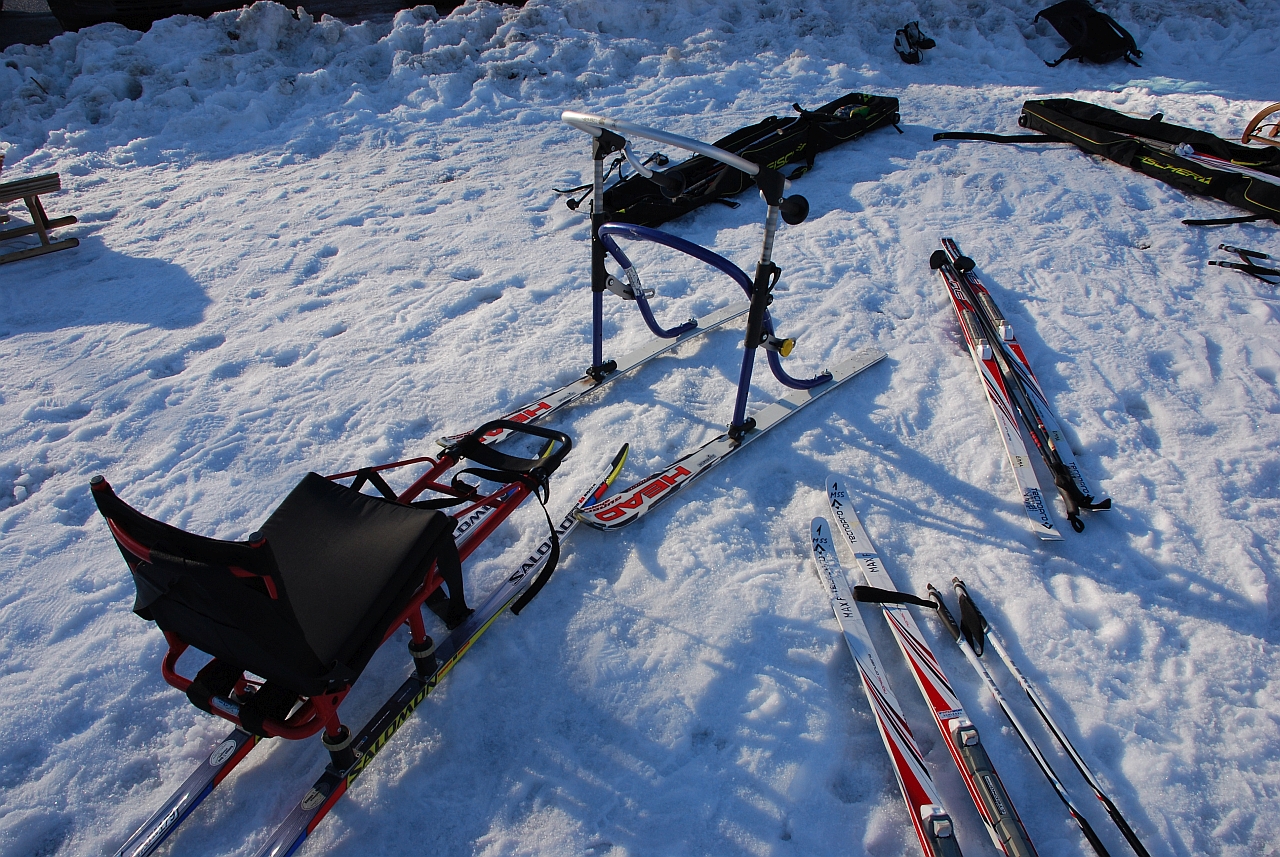 Im Schnee liegen verschiedene Ski und Skistöcke. Ebenso sieht man einen Skilator und einen Skisschlitten