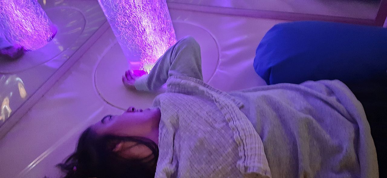 Eine junge Frau liegt an einer beleuchteten Wassersäule. Es leuchtet lila.