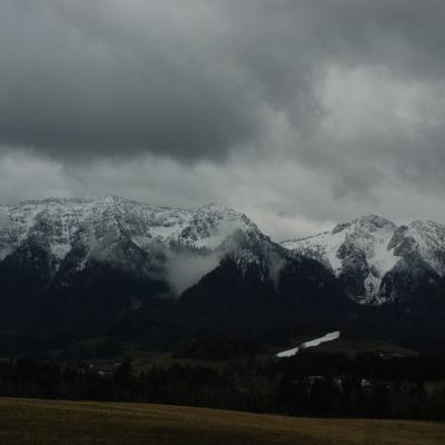 Man sieht eine Bergkette mit weißen Gipfeln. Der Himmel ist mit grauen Wolken verhangen.