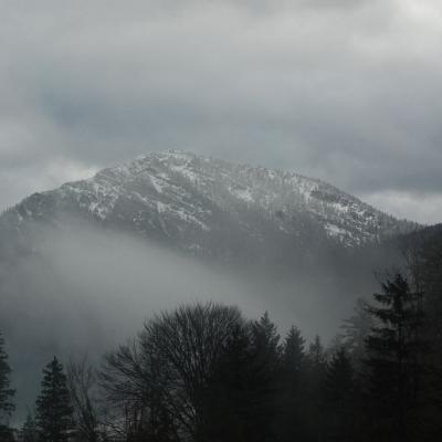 Man sieht eine Bergkette mit weißen Gipfeln. Der Himmel ist mit grauen Wolken verhangen.