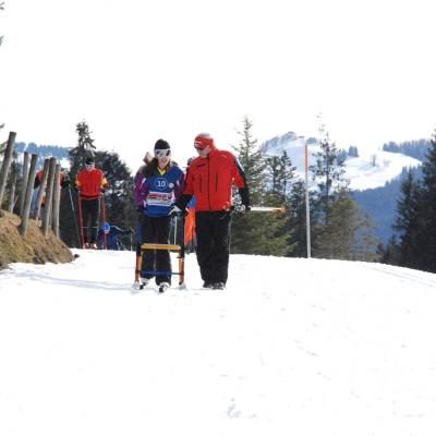 Marija und Martin von der Skiwacht kommen in der Loipe auf die Kamera zu. Im Hintergrund sieht man ein Skigebiet mit Liften.