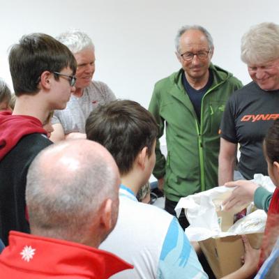 Mehrere Skiwachtler stehen um Florian herum. Gemeinsam mit einem Schüler aus Stuttgart überreicht er eine Kiste mit Geschenken an die Skiwachtler.
