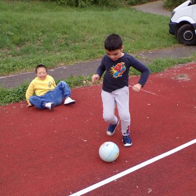 Zwei Schüler spielen auf einem roten Gummiplatz mit einem Fußball.