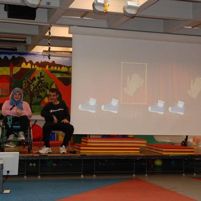 Auf der Bühne in der Aula führt die Klasse 7-9a ihre Body-Percussion auf. Auf der Leinwand sehen alle im Publikum, wie sie mitmachen können.