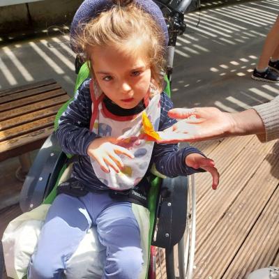 Eva freut sich über den orangefarbenen Schmetterling, der direkt vor ihrem Gesicht ist.