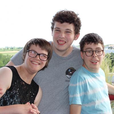 Drei Schüler umarmen sich auf dem Balkon und lachen in die Kamera