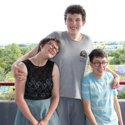 Drei Schüler umarmen sich auf dem Balkon und lachen in die Kamera