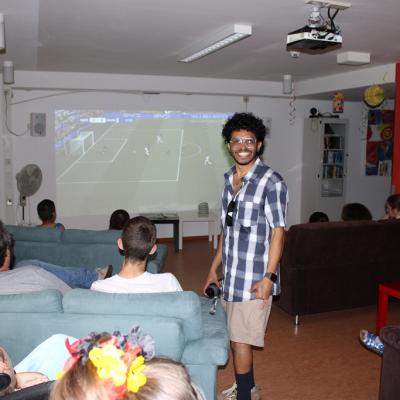 Mehrere Schüler sitzen auf dem Sofa schauen auf die Fußballleinwand , ein Betreuer steht in der Mitte und schaut lachend in die Kamara