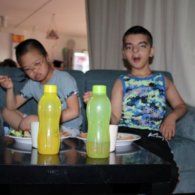 i Schüler sitzen auf dem Sofa vor ihnen stehen Teller mit essen, eine grüne und gelbe Flasche 