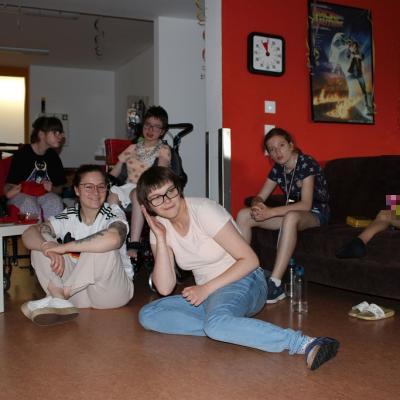Zwei Rollstuhlfahrerinnen ,ein auf dem Sofa sitzende Schülerin, eine Schülerin und eine Betreuerin sitzen auf dem Boden