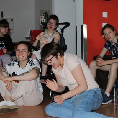 Zwei Rollstuhlfahrerinnen ,zwei auf dem Sofa sitzende Schüler, eine Schülerin und eine Betreuerin sitzen auf dem Boden 