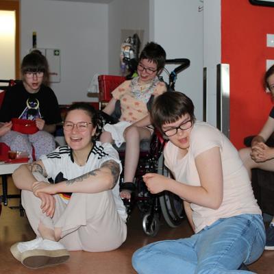 Zwei Rollstuhlfahrerinnen ,ein auf dem Sofa sitzende Schülerin, eine Schülerin und eine Betreuerin sitzen auf dem Boden 