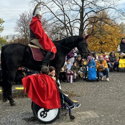 Sankt Martin steht mit seinem halben Mantel mittig im Bild, nach rechts gewandt. Davor der Bettler im Rollstuhl, den anderen halben Mantel um die Schulter gelegt, seine Lehrerin kauert dahinter. Im Hintergrund wieder die Zuschauer.