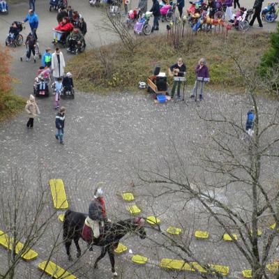 Aufnahme von oben: Sankt Martin zieht mit dem Pferd ins Rondell, die Schulgemeinschaft folgt ihm. Musikanlage und musizierende Kolleginnen sind in der Bildmitte zu sehen.
