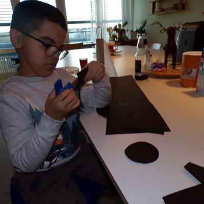 Ein Junge sitzt an einem Tisch. Er schneidet konzentriert mit einer Schere, schwarze Kreise aus Tonpapier aus. 