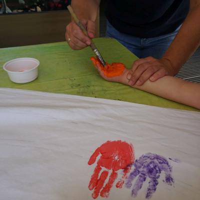 Die Hand eines Kindes wird mit Farbe und Pinsel angemalt.