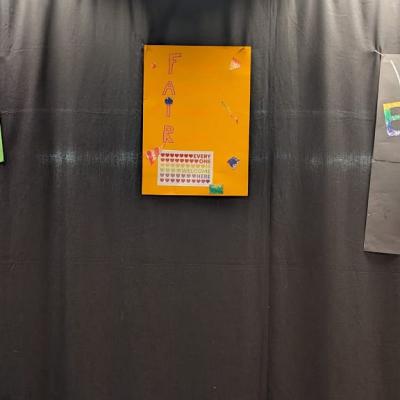 In der Aula hängen drei Plakate an einem Vorhang. Darauf stehen verschiedene Botschaften wie „Mehr Gemeinesam Bewegen!“ oder „Wir sind bunt“.