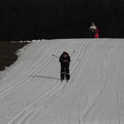 Christopher fährt im Schuss eine Loipe bergab. Oben hinter ihm warten Julian, Lara und Frau Gauch.