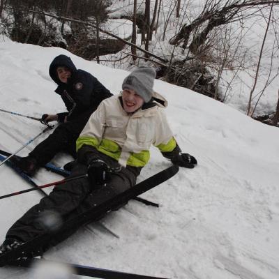 Christopher und Julian liegen im Schnee und lächeln. Sie sind mit ihren Skiern ineinander verkeilt.