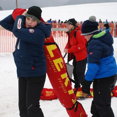 Christopher schultert einen roten Skisack. Josua geht zu ihm, um ihm zu helfen.