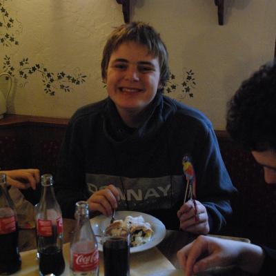 Christopher und Julian sitzen am Tisch im Kannenzimmer. Einer von Beiden isst einen Käsekuchen, der Andere einen Windbeutel mit Schokoladensauce und Vanilleeis.