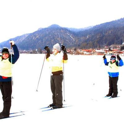 Skifreizeit2025Von links nach rechts sieht man seitlich wie Josua, Julian und Christopher jubeln. Sie halten in ihren Händen die Skistöcke nach oben. Im Hintergrund ein Dorf und bewaldete Berge.montag04