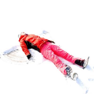 Lara macht einen Schneeengel auf der verschneiten Wiese. Sie liegt auf dem Rücken im Schnee, hat ihre Arme und Beine weit von sich gestreckt