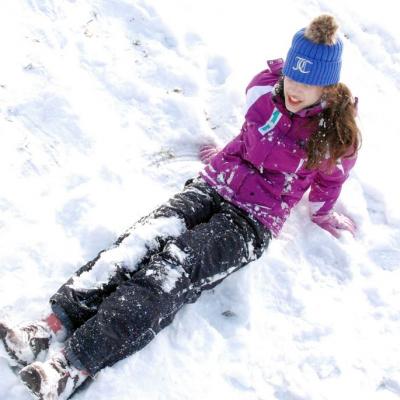 Marija sitzt im Schnee. Die Beine hat sie gerade vor sich ausgestreckt und sie stützt sich hinter ihrem Oberkörper mit ihren Händen ab.