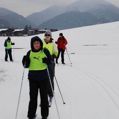 Christopher, Julian und Josua (von vorne nach hinten) fahren auf der linken der beiden Spuren eine Kurve nach links auf der Loipe. Frau Gauch fährt auf der rechten Spur. 