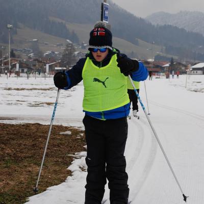 Josua fährt eine Kurve auf der Loipe. Seine Arme mit den Stöcken hat er gerade vor sich. Sein Gesicht sieht konzentriert aus, er trägt eine verspiegelte Sonnenbrille. 