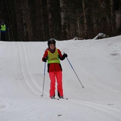 Christopher ist stark gebückt auf seinen Langlaufskiern in der Loipenspur unterwegs. Er stößt sich mit seinen Stöcken im Schnee ab. Er hat für das Rennen seine Skibrille aufgesetzt. 