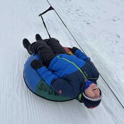 Josua liegt in einem Schlauchreifen und schaut in den Himmel, während er von einem Snowtubinglift den Berg hochgezogen wird. Ringsherum ist Schnee. 
