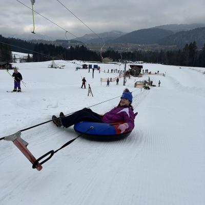 Marija wird vom Snowtubinglift in einem Schlauchreifen den Berg hochgezogen. Im Hintergrund sieht man einen Tellerlift mit Kindern. 