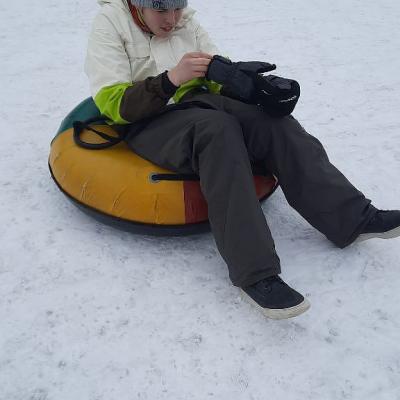 Julian sitzt in einem Schlauchreifen und zieht seine Winterhandschuhe an. 