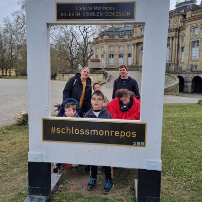 4 Kinder und  2 Erwachsene schauen in die Kamera. Um sie herum ist ein riesiger weißer Bilderrahmen. Auf diesem steht „Schloss Monrepos“