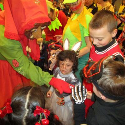 Fasching in der Schulaula, eine Neckarweihinger Mistelhexe verteilt von links Bonbons an 4 verkleidete Kinder im Grundschulalter
