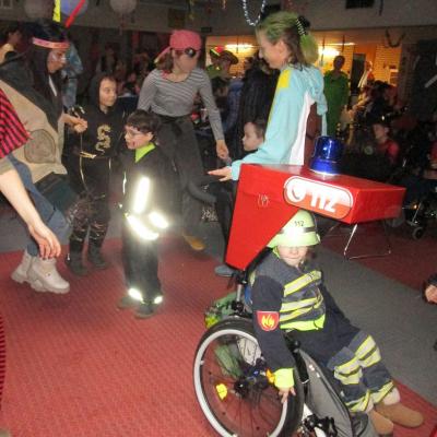 Fasching in der Schulaula, 3 Erwachsene (Indianerin, Piratin, Shiggy) und 3 Kinder im Grundschulalter (Ninja, 2x Feuerwehr, das Kind links im Rollstuhl)