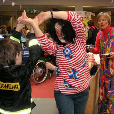 Fasching in der Schulaula, 2 Clowns (Erwachsen) und ein Feuerwehrmann (Kind im Grundschulalter) beim Tanzen