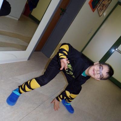 Ein Junge posiert in die Kamera. Er ist in der hocke und eine Hand berührt den Boden. Er trägt ein schwarzes Ninja Köstüm mit gelben Arm und Beinschützern 