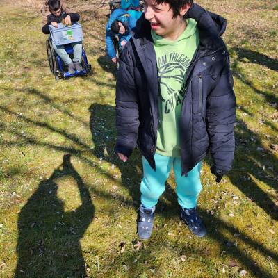 Ein Schüler läuft über die Wiese und sucht lachend das Moos, im Hintergrund ist ein Rollstuhlfahrer mit einer grauen Kiste 
