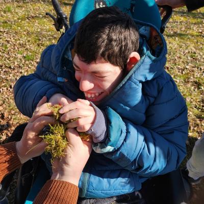 Im Rollstuhl ,lachender Schüler Freud sich über das Moss, Betreuerin gibt Unterstützung 