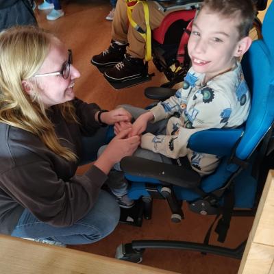 Ein Junge der in einem Stuhl sitzt lächelt in die Kamera. Vor ihm ist eine Frau in der hocke und schaut den Jungen lächelnd an. 