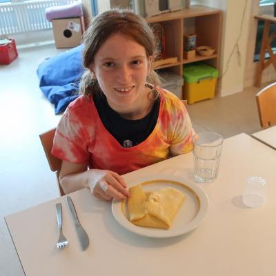 Ein Mädchen sitzt vor einem Teller mit Pfannkuchen und schaut in die Kamera.