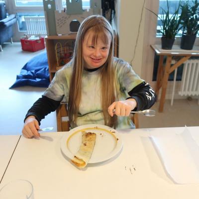 Ein Mädchen sitzt vor einem Teller mit einem belegten Pfannkuchen und lacht in die Kamera.